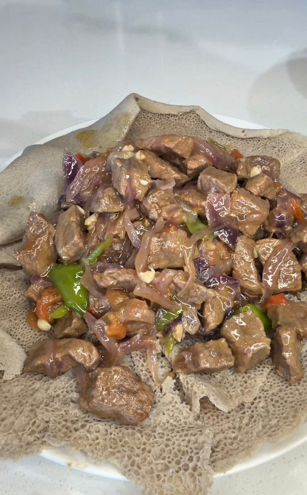 Ethiopian tibs with red onion, green pepper and tomato on injera